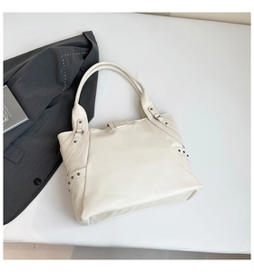 Detail of off-white tote bag showing side leather straps and metal rivets decoration