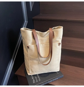 Detail of canvas tote bag showing beige body with brown leather handle and front rivet pocket