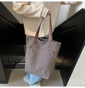 Close-up of canvas tote bag with front pocket, rivet detail and leather handles