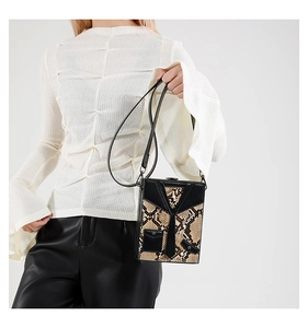 Detail of creative suit-style hard shell crossbody bag featuring snake pattern and tie