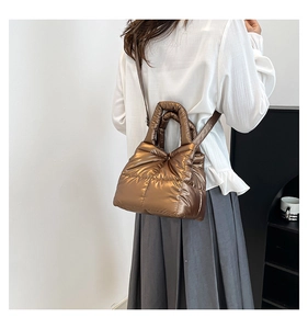 Detail view of coffee-colored quilted puffer bag with metallic finish shown on a model