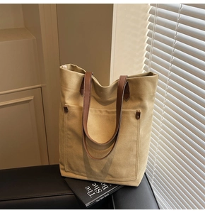 Detail of a khaki canvas tote bag with leather handles and studs on a black leather sofa