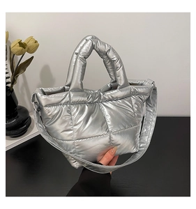 Close-up of a glossy silver quilted puffer bag with dual handles and long shoulder strap