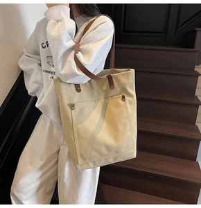 Detail of beige canvas tote bag with premium brown leather straps and rivet hardware