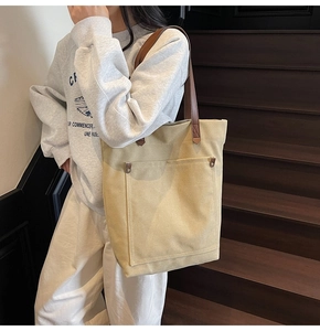 Close-up of beige canvas tote bag featuring brown leather straps and metal rivet pocket