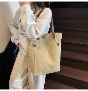 Detail of canvas tote bag showing front pocket with metal rivets and leather straps