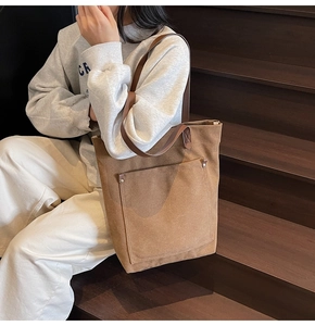 Detail view of brown canvas tote bag with large outer pocket and metal rivet accents