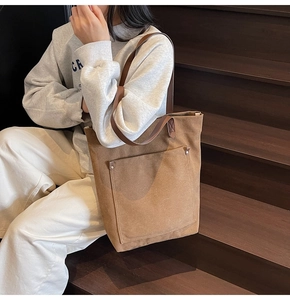 Detail of a large brown canvas tote bag with metal rivet pockets on a wooden background