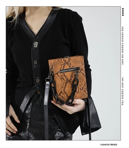 Detail view of stylish orange snake-pattern crossbody bag with chunky black chain decoration