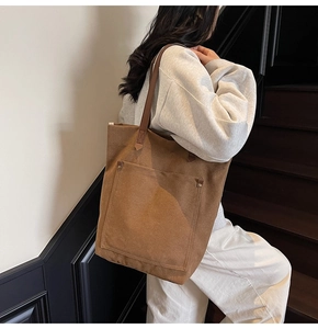 Detailed view of brown canvas tote bag with leather straps and front pocket on model