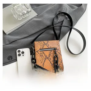 Size comparison of a snakeskin crossbody bag with a smartphone and black chain strap