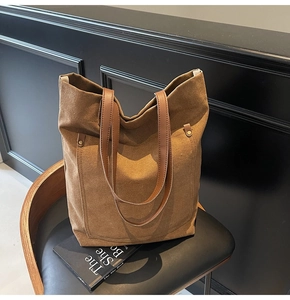 Close-up of brown canvas tote bag with leather handles and metal rivet details on chair