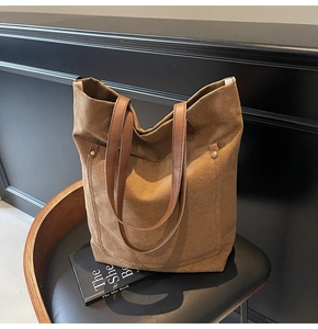 Macro detail of brown canvas tote bag with leather straps and metal rivets on a chair