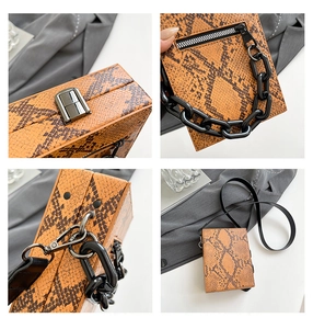 Detail of orange snakeskin crossbody bag with metal lock, chunky chain, and zipper