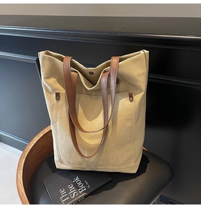 Detail of khaki canvas tote bag featuring brown leather straps and metal rivets