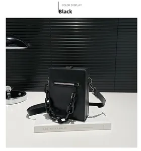 Detail of black crossbody bag featuring silver zipper and bold decorative chain strap