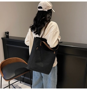 Close-up of black canvas tote bag with brown handles and a large front pocket