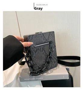 Detail of grey snakeskin texture handbag featuring a bold black chain and zipper pocket