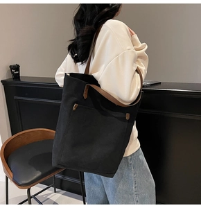 Detail of black canvas tote bag with brown leather handles worn by a model in a cafe