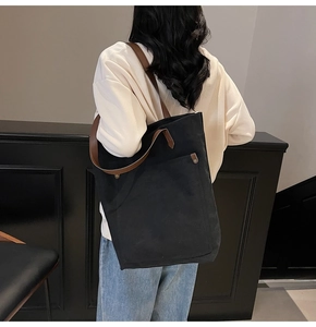 Detail of black canvas tote bag showing dark brown leather straps and metallic rivets
