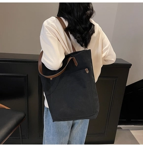 Detalle de un bolso tote de lona negra con correas marrones y bolsillo de remaches metálicos
