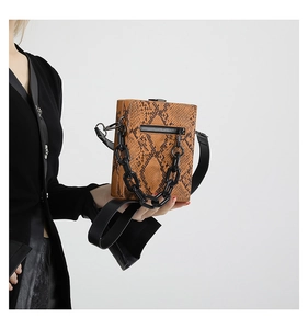 Detail of snake pattern leather crossbody bag with chunky black resin chain and metal lock