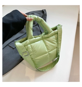 Detail of light green quilted down tote bag fabric with silver metal buckle on grey blazer