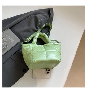 Macro shot of light green quilted down tote bag with wide strap and phone for scale