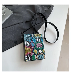 Detail of a square hardshell box bag with vibrant multi-color snakeskin print and black strap
