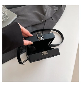 Detailed view of black hard shell box bag being opened showing silver metal clasp and lining
