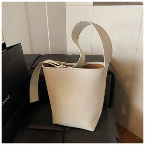 Detail der cremeweißen Beuteltasche aus Leder mit Narbung auf einem schwarzen Sofa