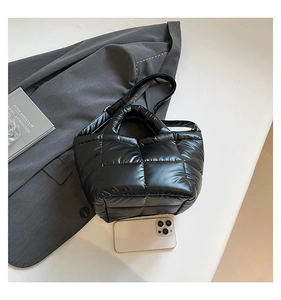Macro detail of black quilted puffer tote bag with adjustable strap and smartphone for scale