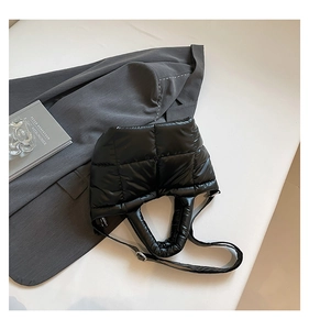 Detail of black quilted puffer tote bag with glossy finish and silver hardware on neutral background