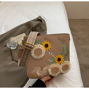 Close-up of floral embroidery on a brown shoulder bag with a woven geometric strap