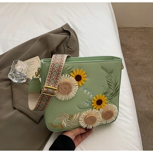 Detail of light green crossbody bag with floral embroidery and wide geometric strap