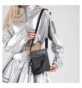 Detail of dark grey snakeskin crossbody bag with thick black chain on a model