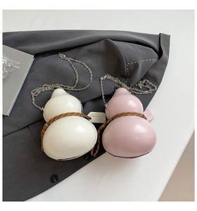 Detail of pink and white gourd-shaped crossbody bags with metal chains on a grey suit