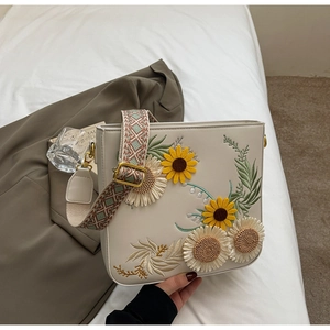 Detailed close-up of sunflower embroidery and ethnic jacquard strap on cream white bag