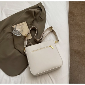 White crossbody bag with jacquard strap and gold zipper detail on fabric surface