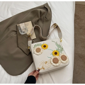 Close-up of 3D sunflower embroidery and woven strap on a white crossbody bag