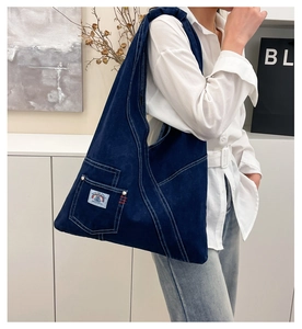 Detail of dark blue washed denim tote bag with white stitching and front pocket