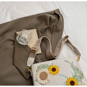 Close-up of sunflower embroidery and woven shoulder strap on a white crossbody bag