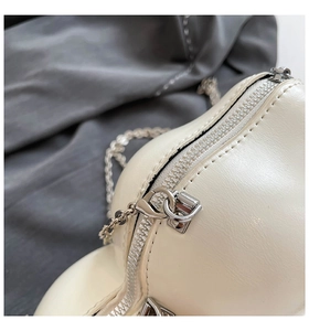 Detail of silver metal zipper and chain strap on a creamy white designer crossbody bag