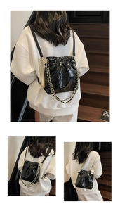 Detail of black quilted leather bucket bag with gold chain strap on a wooden staircase
