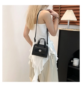 Detail of black leather crossbody bag with silver twist lock on a modern lifestyle model