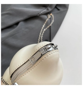 Detail of silver zipper and fine metal chain on a creamy white leather sling bag