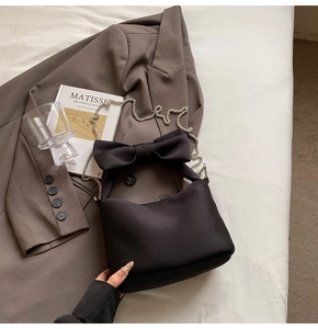 Close-up of black bow handbag with silver chain on brown blazer and art book background