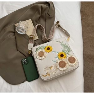 Detail of floral sunflower embroidery and wide patterned strap on beige crossbody bag