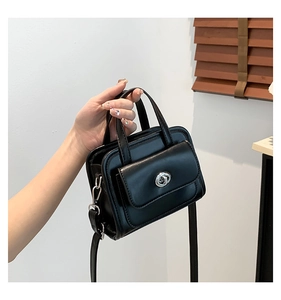 Close-up of black leather handbag featuring a silver twist lock pocket and top handles