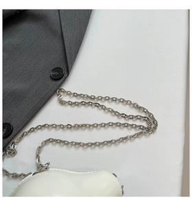Detailed close-up of glossy white heart-shaped shoulder bag with silver metal chain strap